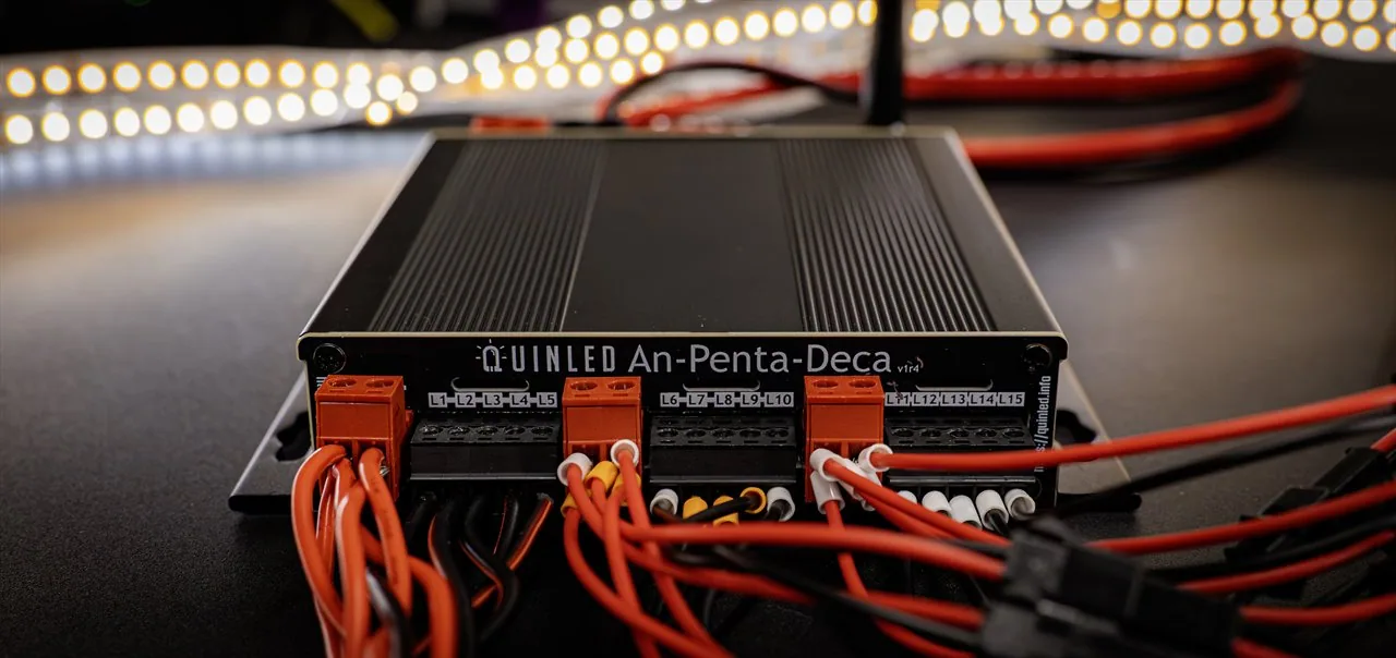 QuinLED An-Penta-Deca finned case front-on, fifteen L1-L15 outputs wired with ferruled red cables and lit warm-white LED strips behind
