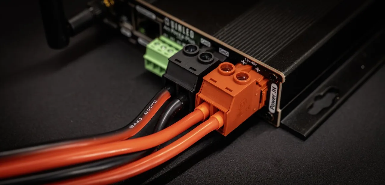 QuinLED An-Penta-Plus Power IN close-up, orange and black plug terminals fed by thick red and black 12AWG wires into the finned case