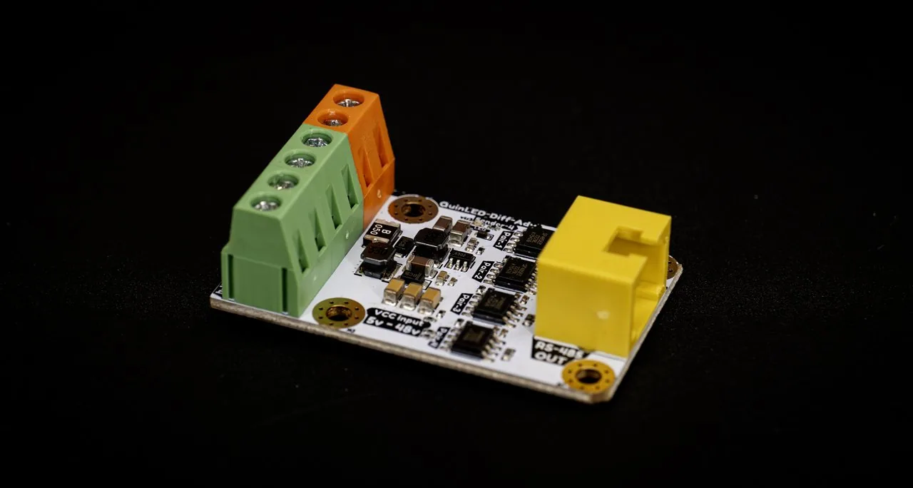 QuinLED Diff-Adv sender board on a dark background, green and orange screw terminals, yellow RJ45 jack and multiple RS-485 chips on white PCB