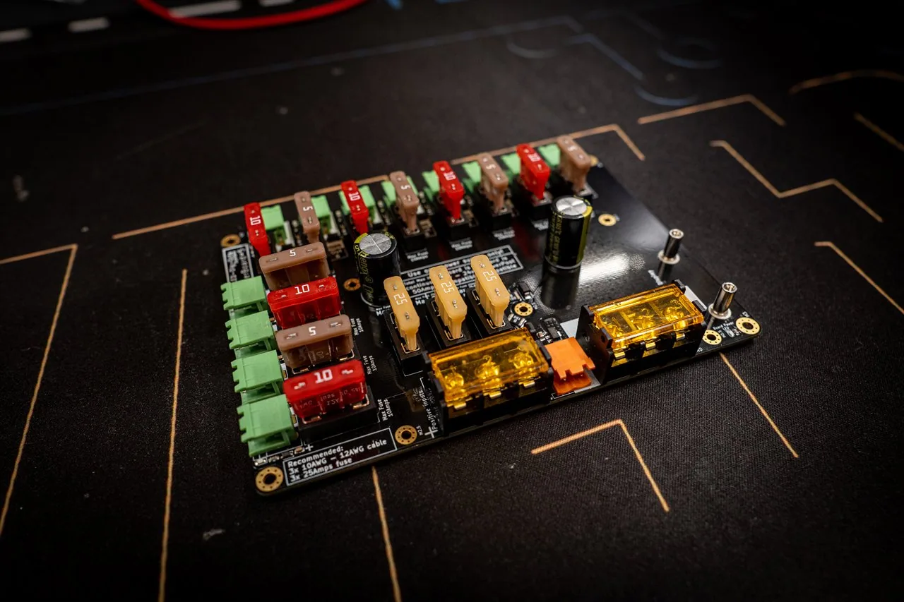 QuinLED Dig-Octa Power-5 at an angle, black Powerboard with blade fuses, gold bolt input terminals and an orange connector on a dark mat