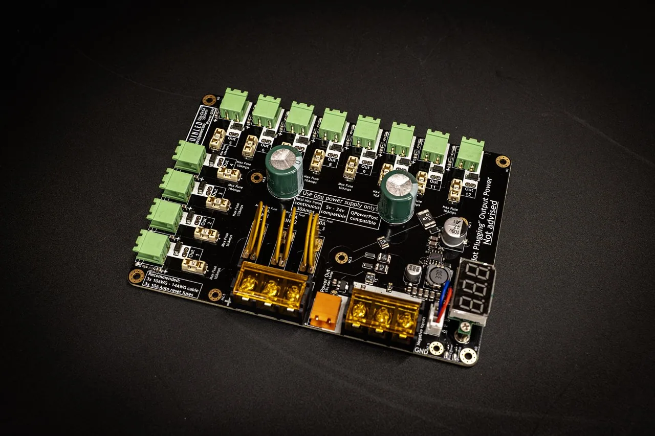 QuinLED Dig-Octa Power-5HV at an angle, dark board with green terminals, large capacitors, gold bolt inputs and a voltage display