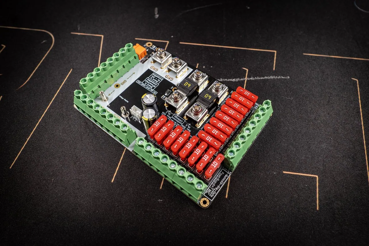 QuinLED Dig-Octa Power-7HC at an angle, board with green screw terminals, red blade fuses and high-current bolt terminals on a dark mat