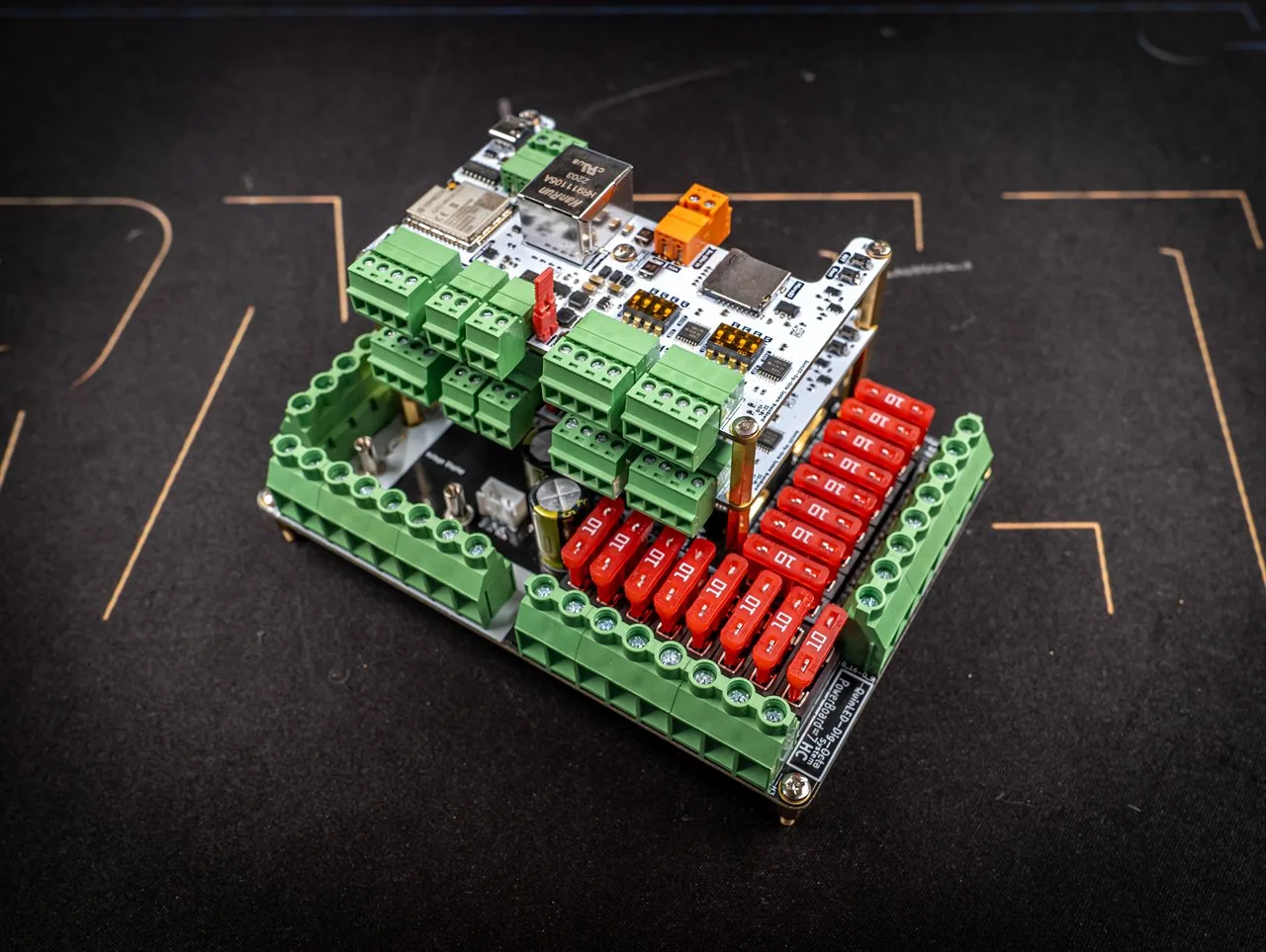 QuinLED Dig-Octa System, angled view of one assembled Brainboard-on-Powerboard unit with green terminals and red blade fuses on a dark mat