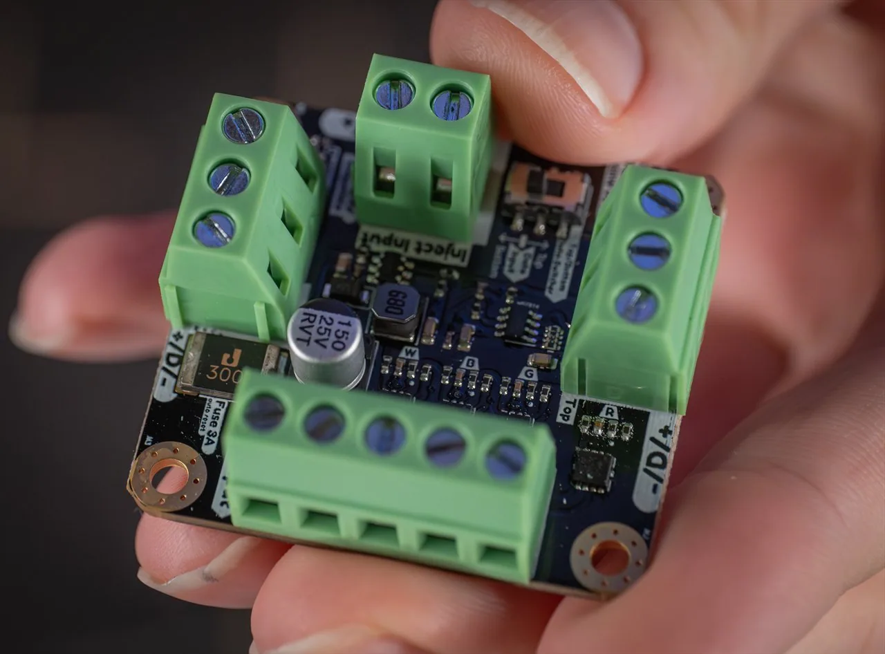 QuinLED dig2analog board held in fingers, angled macro of green screw terminals, an inductor and a 150uF capacitor on black PCB